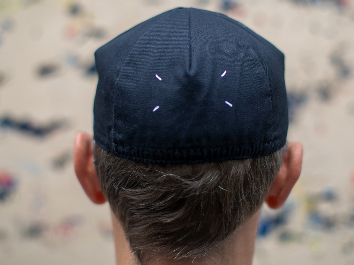 Rear view of the Blue Lug Maison Cycle Cap in black, showing four white stitches arranged on the crown — a nod to a certain famous fashion house.