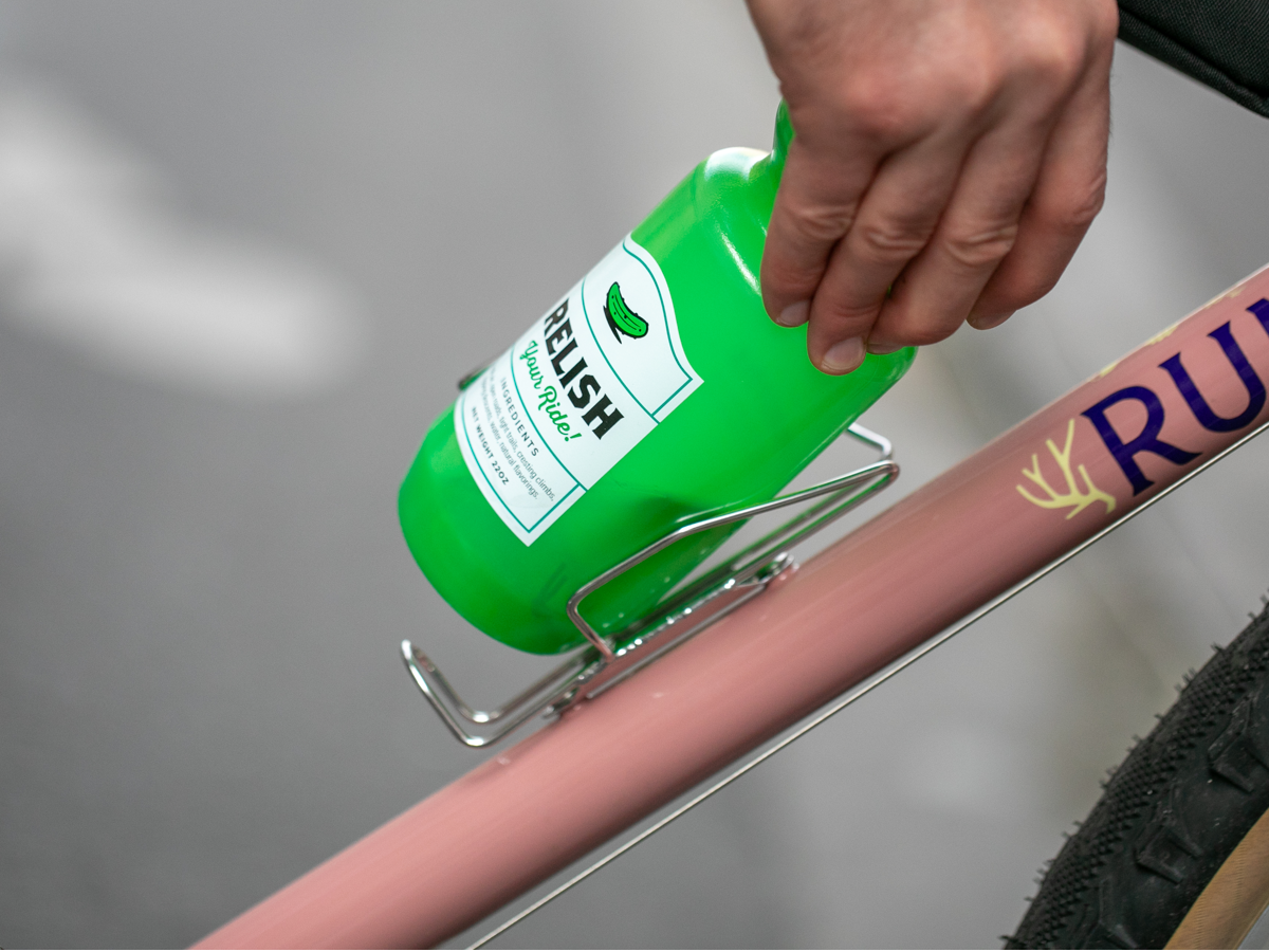 Main retirant un bidon d’un porte-bidon à chargement latéral Velo Orange Crescent sur un cadre de vélo rose