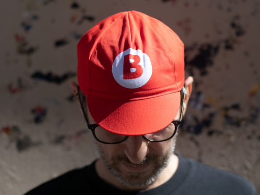 Casquette de cyclisme Blue Lug Jump and Dash rouge, portée visière baissée, vue de face. Un grand cercle blanc avec le logo "B" rouge — clin d'œil à un certain plombier célèbre — orne le panneau avant.