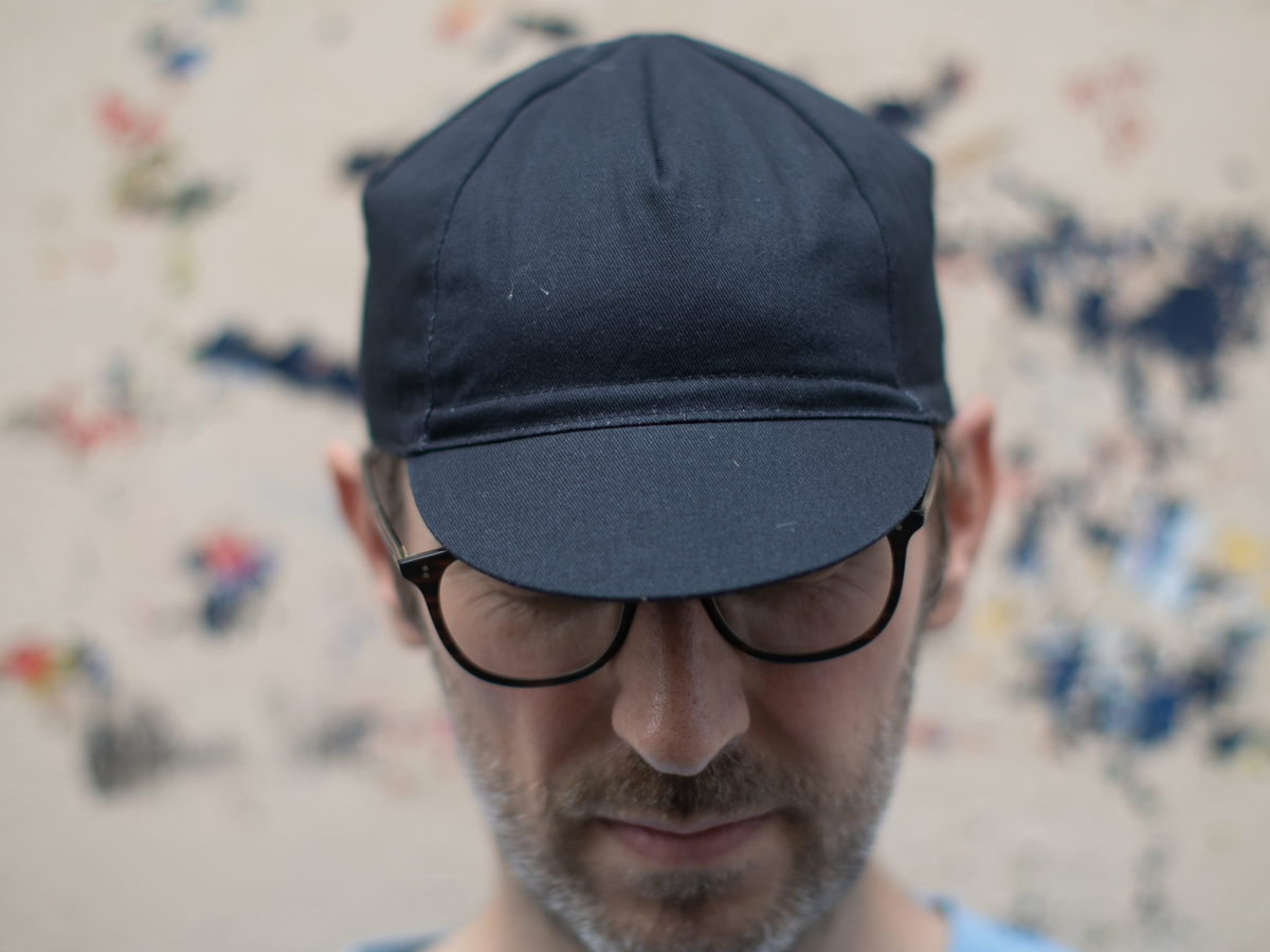 Casquette de cyclisme Blue Lug Maison coloris noir, portée visière baissée, vue de face. Le panneau et la visière unis ne laissent rien deviner.