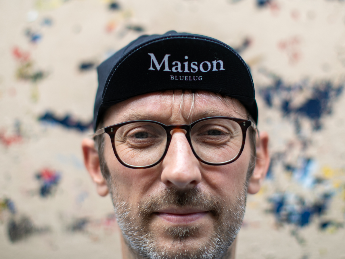 Casquette de cyclisme Blue Lug Maison coloris noir portée visière relevée, vue de face. "Maison BLUELUG" est brodé en lettres grises sérif sur la visière noire.
