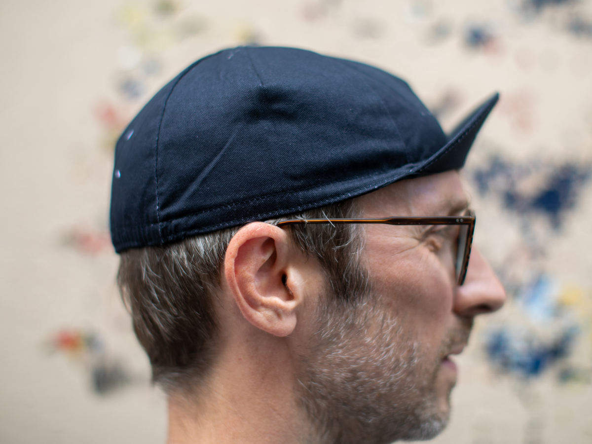 Profil de la casquette de cyclisme Blue Lug Maison coloris noir, montrant le tissu uni et la silhouette pointue caractéristique de la casquette cycliste.