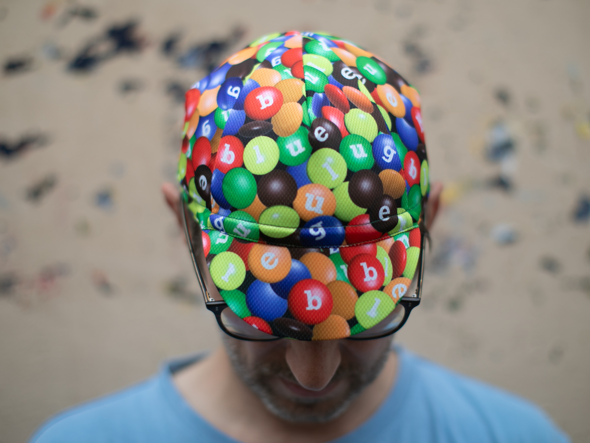 Casquette de cyclisme Blue Lug coloris Chocolate/Poly, vue de dessus. L'imprimé all-over de bonbons chocolatés colorés avec les lettres Blue Lug recouvre l'intégralité de la casquette.
