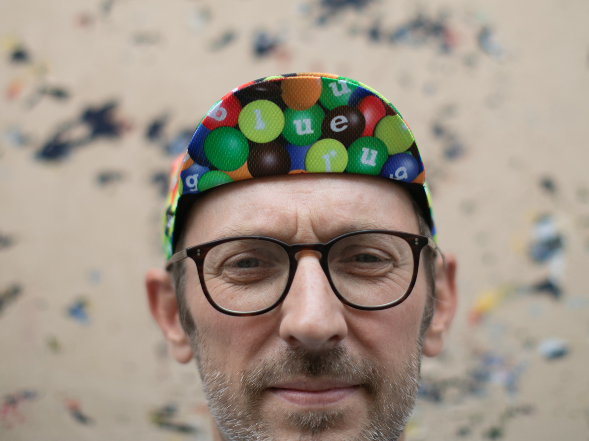 Casquette de cyclisme Blue Lug coloris Chocolate/Poly portée visière relevée. L'imprimé bonbons et les lettres Blue Lug sont visibles sur les panneaux avant.