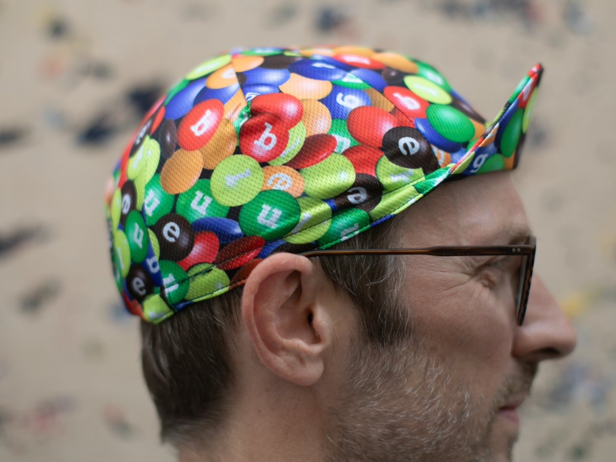 Vue de profil de la casquette de cyclisme Blue Lug coloris Chocolate/Poly, montrant la silhouette classique de la casquette cycliste et l'imprimé all-over bonbons chocolatés.