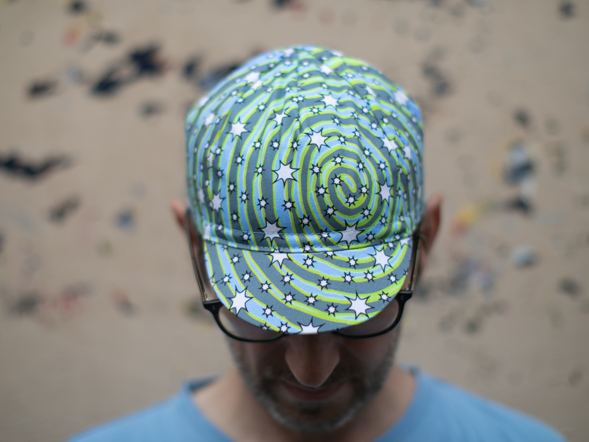 Blue Lug Cycle Cap in Dreamer, seen from above. The all-over swirl print in blue, grey and neon yellow-green with white stars covers the entire cap.