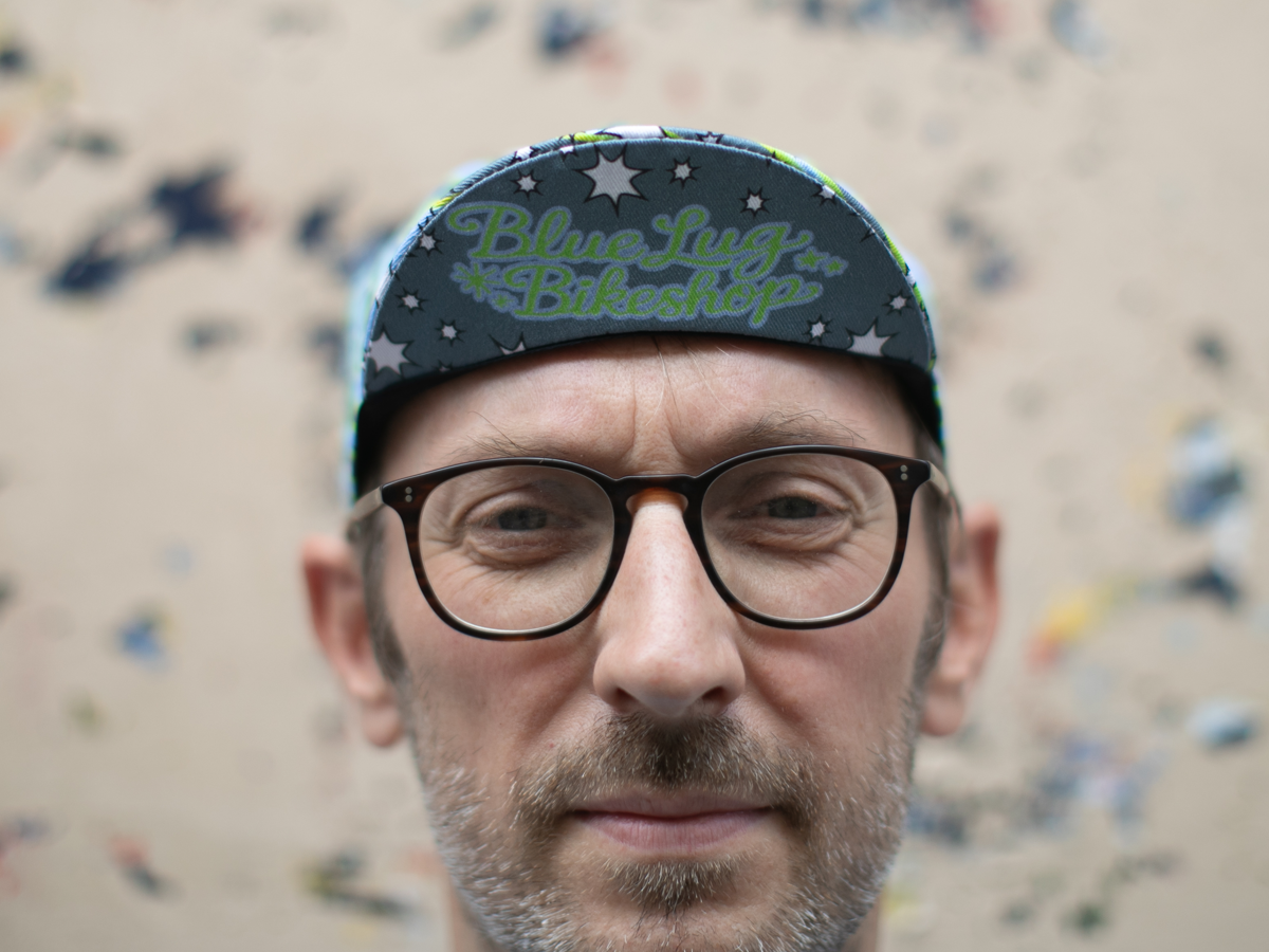 Blue Lug Cycle Cap in Dreamer worn brim-forward, front view. The dark brim features "Blue Lug Bikeshop" in retro green script on a starry background.