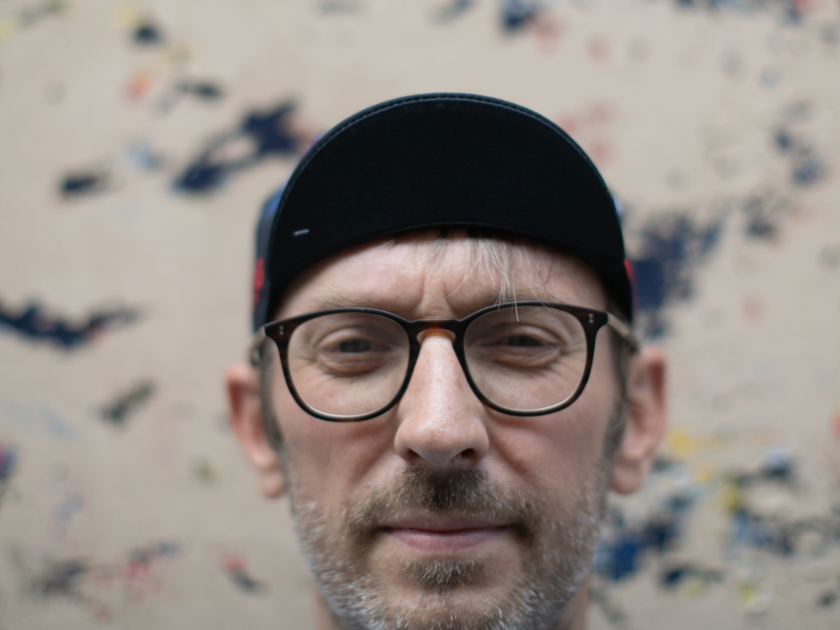 Blue Lug Original Cycle Cap in black worn brim-down, front view. The plain black brim and geometric side panels are visible.