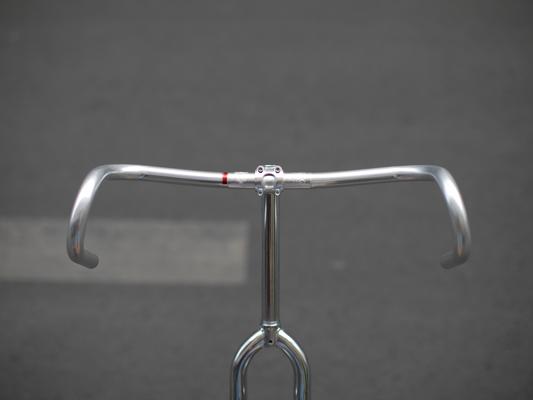 CRUMB x NITTO Futen Drop handlebar front view, polished silver, showing wide flared drop profile and red clamp accent on a chrome stem and fork