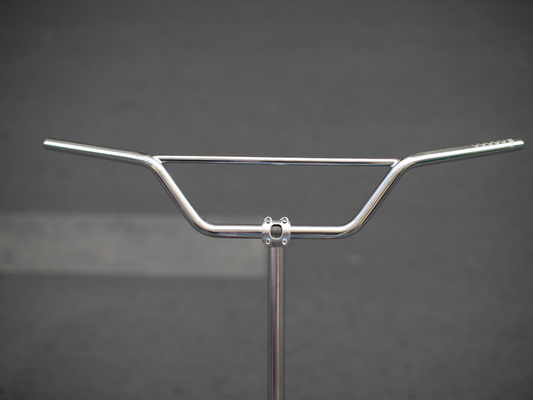 Magic Components Noppo Bar, front view. Chrome CrMo steel handlebar with prominent rise and crossbar brace, shown mounted on a display stand against a grey background.