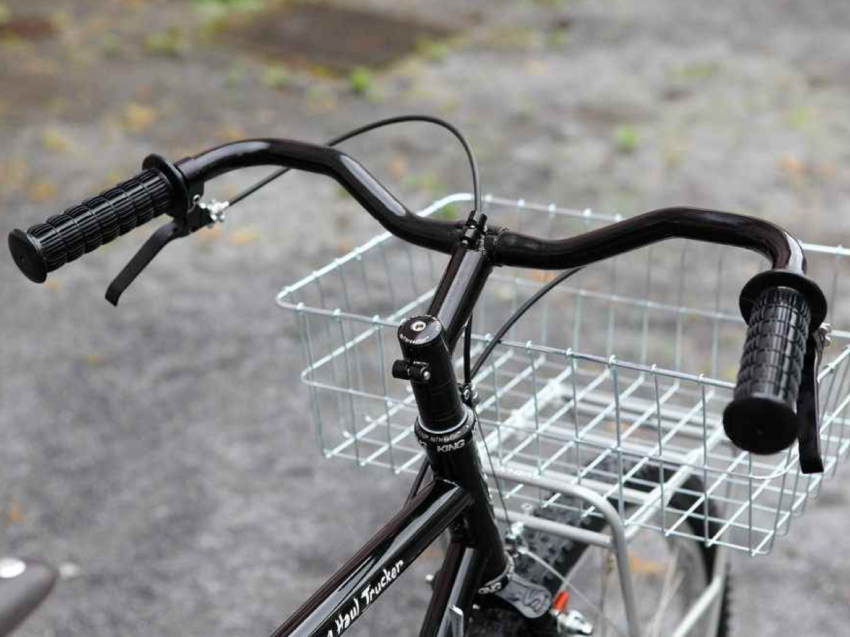 Guidon Nitto B356 monté sur un vélo de ville noir en position promenade haute, avec poignées caoutchouc noires, leviers de frein inversés et panier avant Wald.