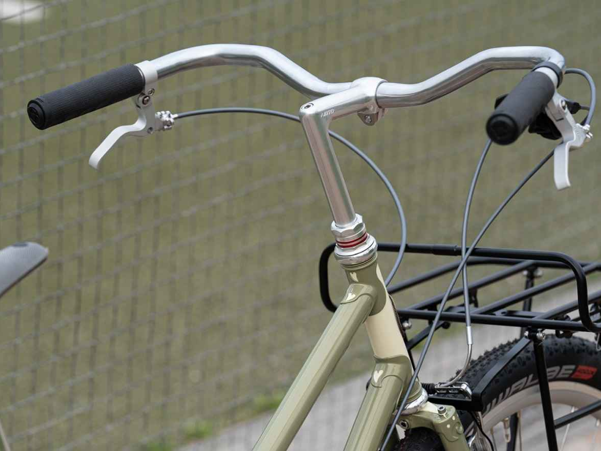 Nitto B356 handlebar in silver installed on an olive commuter bike with a Nitto stem, reverse brake levers, and a front rack, in the upright promenade position.