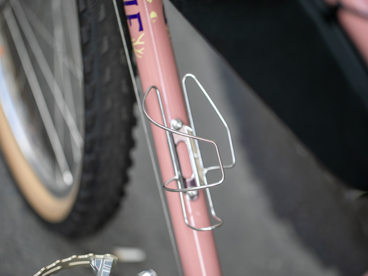 Porte-bidon à chargement latéral Velo Orange Crescent monté sur le tube diagonal d’un vélo rose, sans bidon