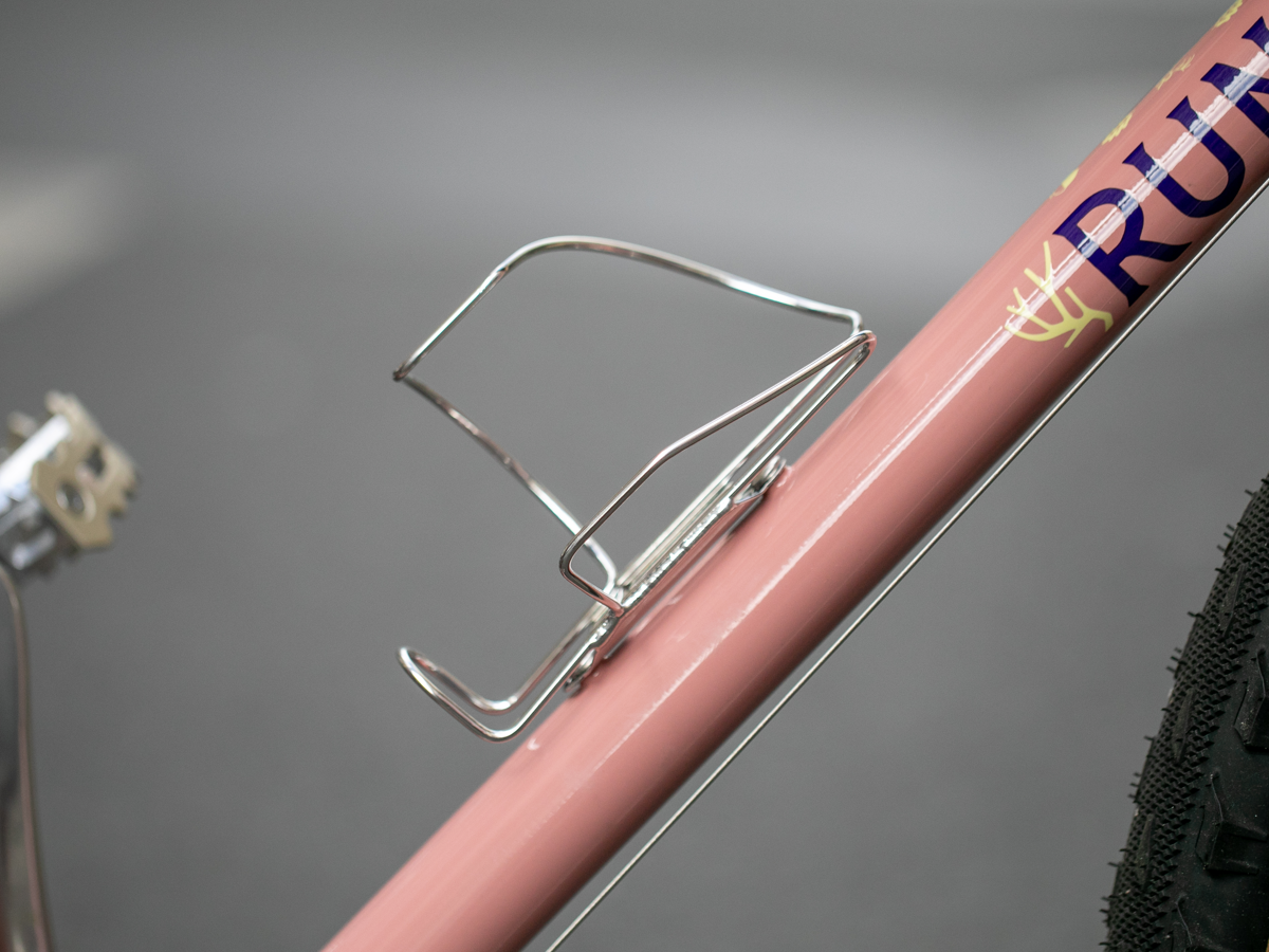 Porte-bidon à chargement latéral Velo Orange Crescent monté sur le tube de selle d’un vélo rose, vue détail sans bidon
