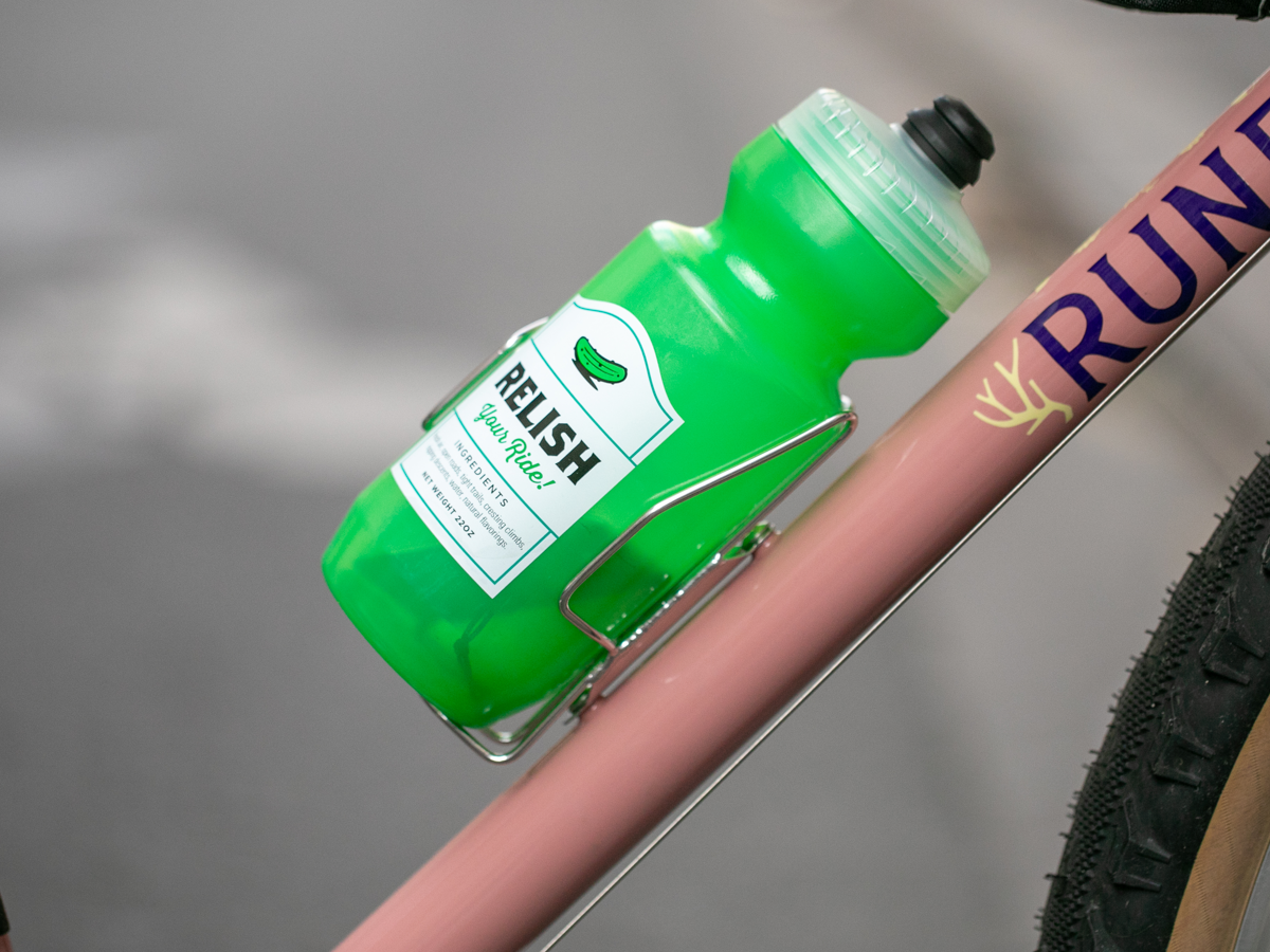 Bidon vert maintenu dans un porte-bidon à chargement latéral Velo Orange Crescent sur un vélo rose